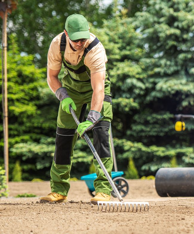 Gärtner mit grüner Cap und Arbeitskleidung hackt Boden